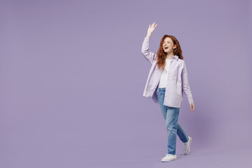 Full size body length happy young redhead curly woman 20s wears white T-shirt violet jacket go meet greet wave hand as notices someone isolated on pastel purple color wall background studio portrait.