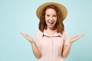 Surprised smiling cheery young redhead woman wears casual pink dress straw hat look camera spread hands say wow omg isolated on pastel blue color background studio portrait. People lifestyle concept