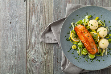Portion of fried salmon, served with mashed potatoes and cooked leek. Top view. Gray plate, wooden background.