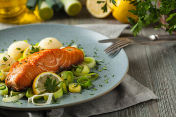 Portion of fried salmon, served with mashed potatoes and cooked leek. Front view. Gray plate, wooden background.