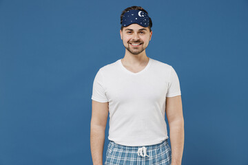 Calm smiling caucasian happy fun young man 20s wearing pajamas jam sleep mask white t-shirt resting relaxing at home looking camera isolated on dark blue background Good mood night bedtime concept