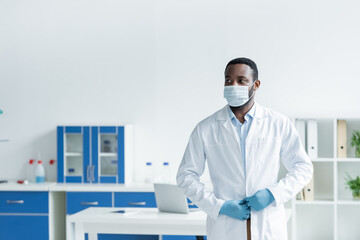 Fototapeta premium African american scientist in medical mask adjusting white coat in lab