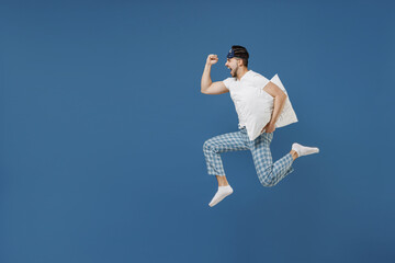 Full length side view young man 20s wearing pajamas jam sleep mask resting relaxing at home jump...
