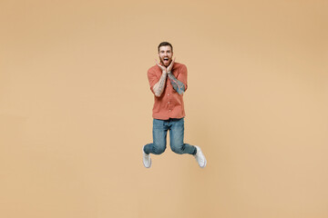Fototapeta na wymiar Full size body length laughing humorous pampering tatooed young brunet man 20s short haircut open mouth wears apricot shirt jump spreading hands isolated on pastel orange background studio portrait