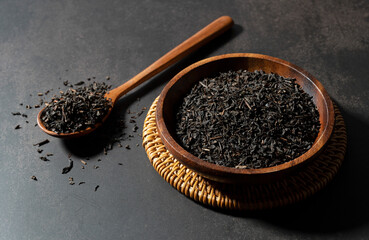 Tea leaves in a spoon with a wooden plate on a black background