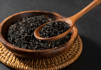 Tea leaves in a spoon with a wooden plate on a black background
