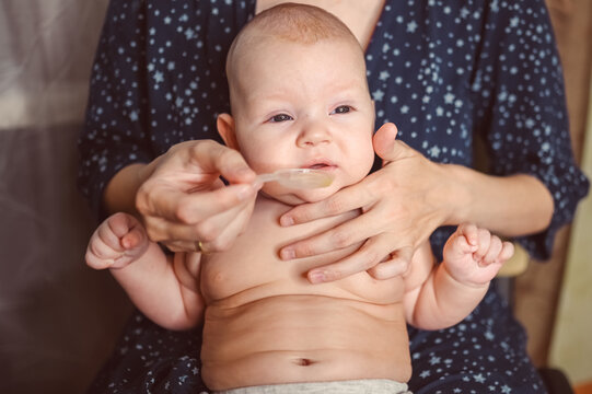 Mother And Newborn Funny Emotional Crying Infant Naked Baby Boy Takes Liquid Medication Or Antipyretic Medicine Syrup From Spoon. Healthy Child, Concept Of Hospital And Happy Motherhood. Nursery