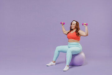Full length fun side view young chubby overweight plus size big fat fit woman in red top warm up train with dumbbells sit fit ball isolated on purple background gym Workout sport motivation concept