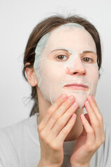 Portrait of a woman with a moisturizing paper mask on her face. Facial skin care, beauty procedures