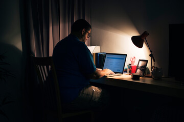 Man working in a dark home office with a laptop - Powered by Adobe