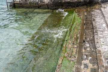 lake clear water surf on landing stage at village on lake shore, Torno,  Como, Italy