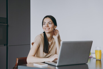 Young happy freelenacer copywriter housewife woman 20s in beige shirt eat breakfast using laptop pc...