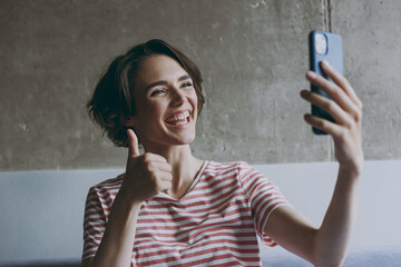 Cropped up photo shot young in casual clothes sit on grey sofa doing selfie shot mobile cell phone post photo social network show thumb up rest indoors flat at home People lifestyle leisure concept.