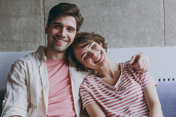 Young smiling satisifed happy couple two friend woman man 20s in striped tshirt casual clothes sitting on sofa boyfriend hugs girlfriend resting indoors at home flat together People lifestyle concept