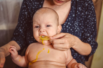 Mother and newborn funny emotional crying infant naked baby boy takes liquid medication or...