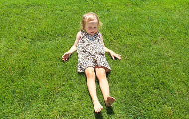 Happy little girl lying on grass. Smiling baby child full length on green lawn.