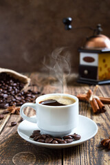 Hot steaming coffee on an old wooden table with coffee beans, manual coffee grinder. Vertical view