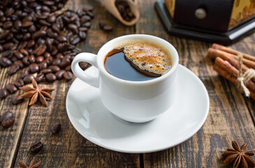 Hot coffee on a wooden background with coffee beans, manual coffee grinder, cinnamon sticks.