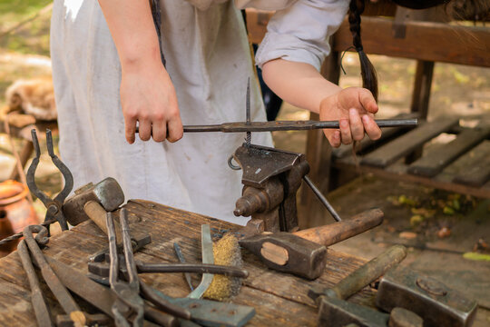 Professional blacksmith woman in historical costume working with metal on anvil at outdoor workshop - close up view. Handmade, reenactment, craftsmanship, medival concept