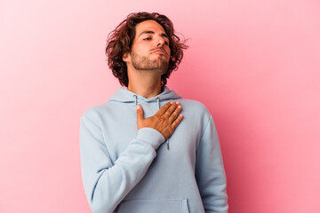 Young caucasian man isolated on pink bakcground taking an oath, putting hand on chest.