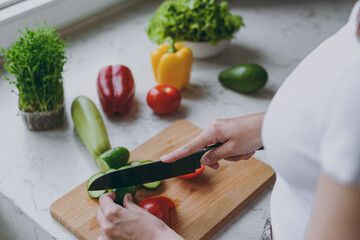 Close up caucasian female hands in casual white clothes prepare vegetables salad on cutting board...