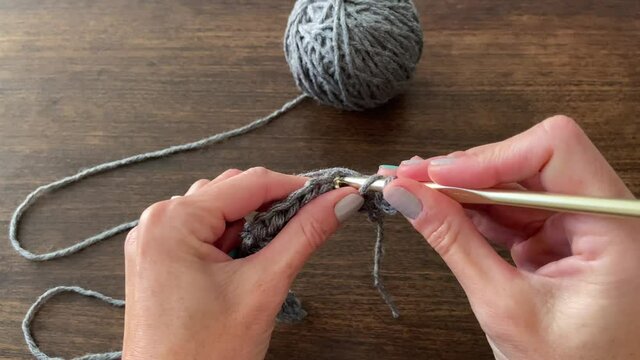 An adult woman knitting with a hook and gray thread shot in 4K