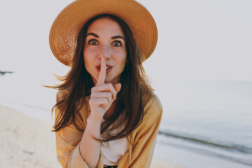 Close up surprised traveler tourist young woman in straw hat shirt summer clothes say hush quiet...