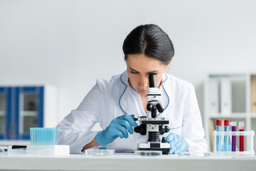 Scientist in latex gloves using microscope near test tubes with samples in lab