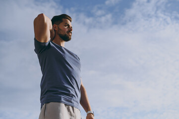 Bottom view young strong sporty athletic toned fit sportsman man in sports clothes warm up training doing hand exercise rest at sunrise sun over sea beach outdoor on pier seaside in summer day morning