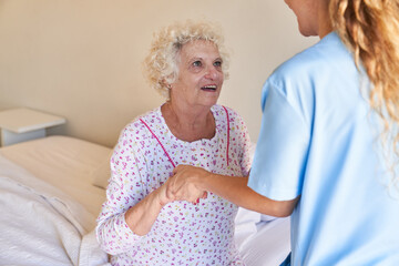Altenpflegerin hilft alter Frau beim Aufstehen vom Bett