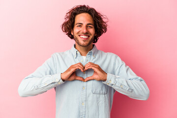 Young caucasian man isolated on pink bakcground smiling and showing a heart shape with hands.