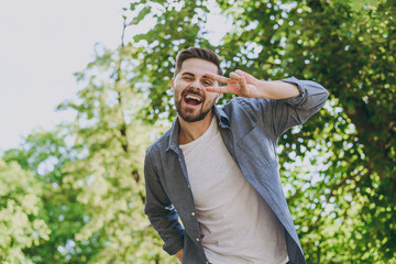 Bottom view young happy man in blue casual shirt t-shirt walk cover eye with v-sign rest relax in spring green city park go down alley sunshine lawn outdoors on nature Urban lifestyle leisure concept.