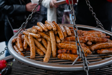 Process of grilling fresh long meat sausages on big round hanging grill at summer local food market: close up view. Outdoor cooking, barbecue, gastronomy, cookery, street food concept