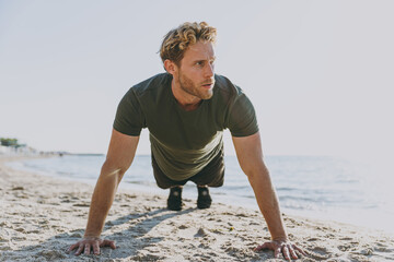Full size front view young sporty athletic toned fit sportsman man wearing sports clothes warm up training in push up position at sunrise sun dawn over sea beach outdoor seaside in summer day morning.
