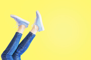 Female legs in pose on yellow background. Woman feet in jeans and striped sneakers with copy space