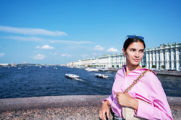 Fototapeta na wymiar Pretty young lady wearing pink shirt with beige handbag standing at city street