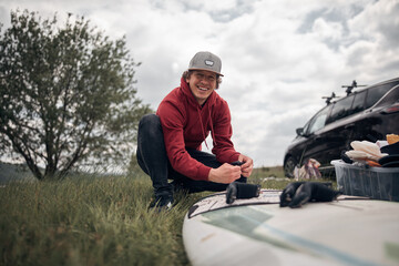 Obraz premium Windsurfer and camper packing and unpacking from a car's roof rack in nature.