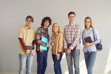 Obraz premium Positive happily smiling male and female teenage students group portrait isolated on grey copy space background. Stylish good-looking young people with studying stationary full length studio shot