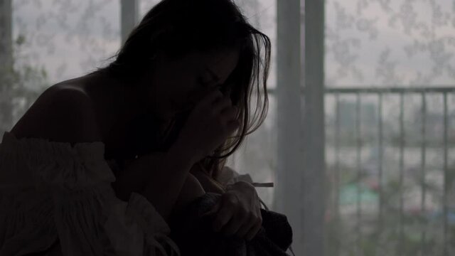 Depressed Asian woman sitting alone on the bed in the dark with cuddle herself and crying. Loneliness sad female think grief trouble life problem in bedroom. Negative emotion and mental health concept