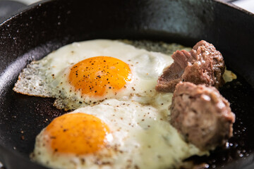 Eggs are fried with pieces of meat in a cast-iron pan.