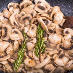 Mushrooms are fried with rosemary - sliced champignons in a pan close-up