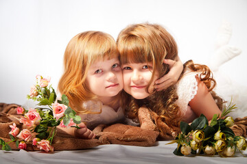 Cute girls in beautifull dress with flowers in the studio on a white background. Young sisters posing indoors