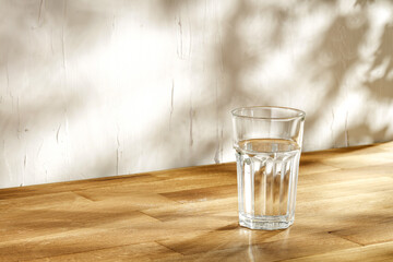 Glass of water on desk and wall with shadows 