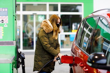 Woman wear medical mask at self-service gas station, hold fuel nozzle, refuel the car with petrol...