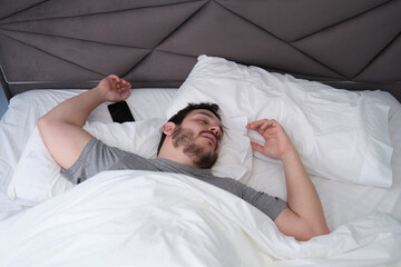 Young latin man sleeping spread out in bed with his smartphone. Sleep position concept.