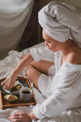 beautiful girl with a towel on her head sits in bed and has breakfast with a healthy sandwich with coffee