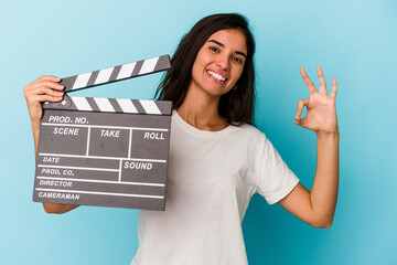 Young caucasian woman holding a clapperboard isolated on blue background cheerful and confident...