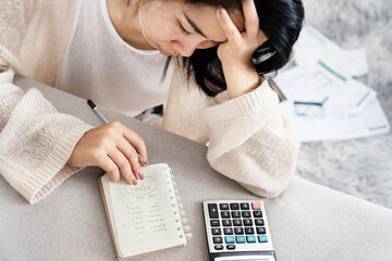 stress Asian woman calculating her debt having problem with loan looking at list of expenses on...