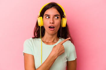 Young caucasian woman listening music isolated on pink background pointing to the side