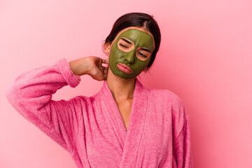 Young caucasian woman wearing a bathrobe and facial mask isolated on pink background touching back of head, thinking and making a choice.